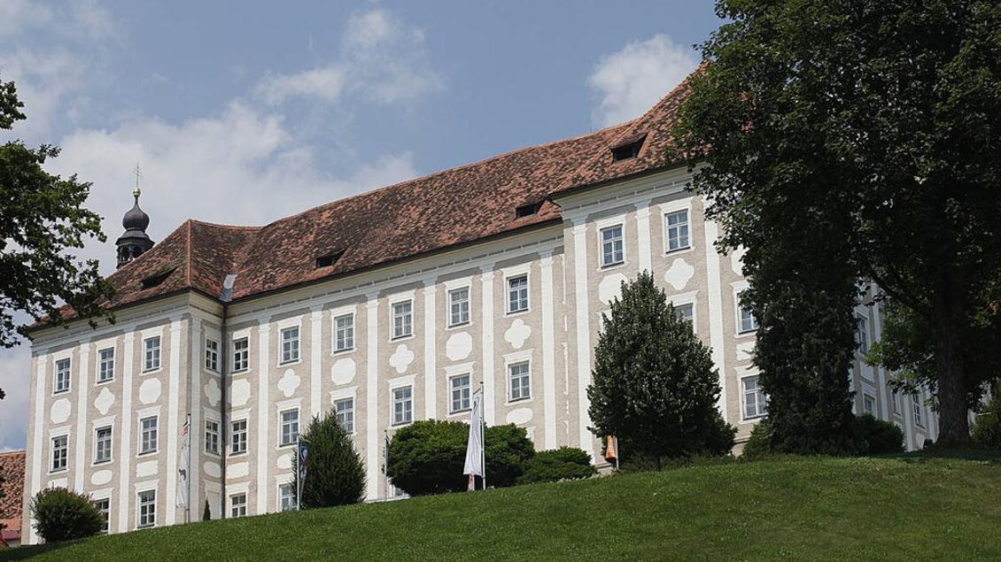 Ein imposantes Gebäude mit einer weißen Fassade und roten Dächern. Das Schloss liegt auf einem Hügel, umgeben von Bäumen und Grünflächen. | © Enrico Caracciolo