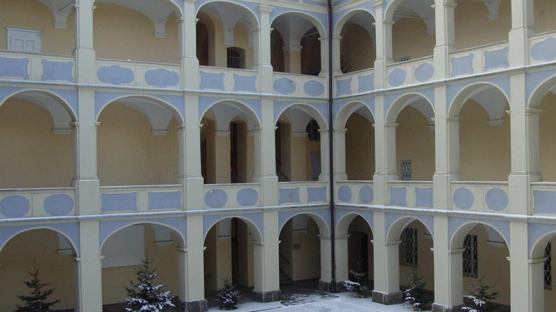 Ein Innenhof mit hohen, gebogenen Bögen und einer schneebedeckten Fläche. Die Wände sind in sanften Gelbtönen gehalten und es gibt einige kleine Bäume. | © www.piber.com