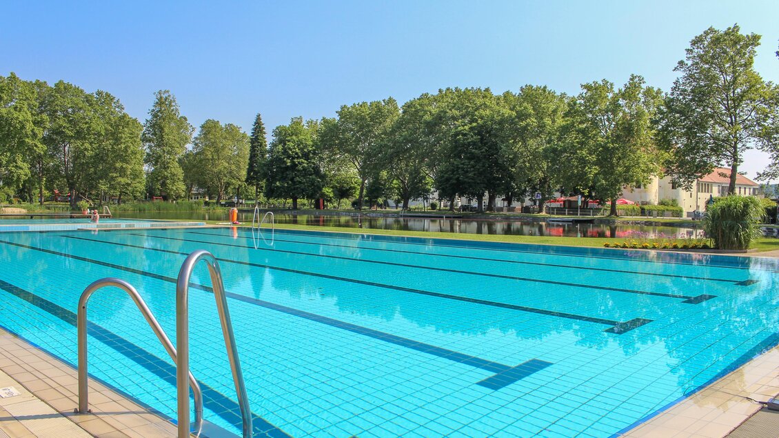 Ein schön gestalteter Swimmingpool mit klarem Wasser und umgebenden Bäumen. Es ist ein sonniger Tag mit blauem Himmel. | © Sandra Brünner