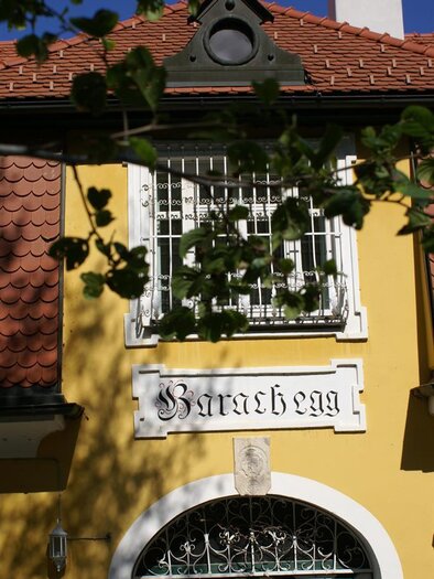 A historic building with a yellow facade and a red roof. Above the entrance is the inscription "Barachegg". | © Karl Oswald