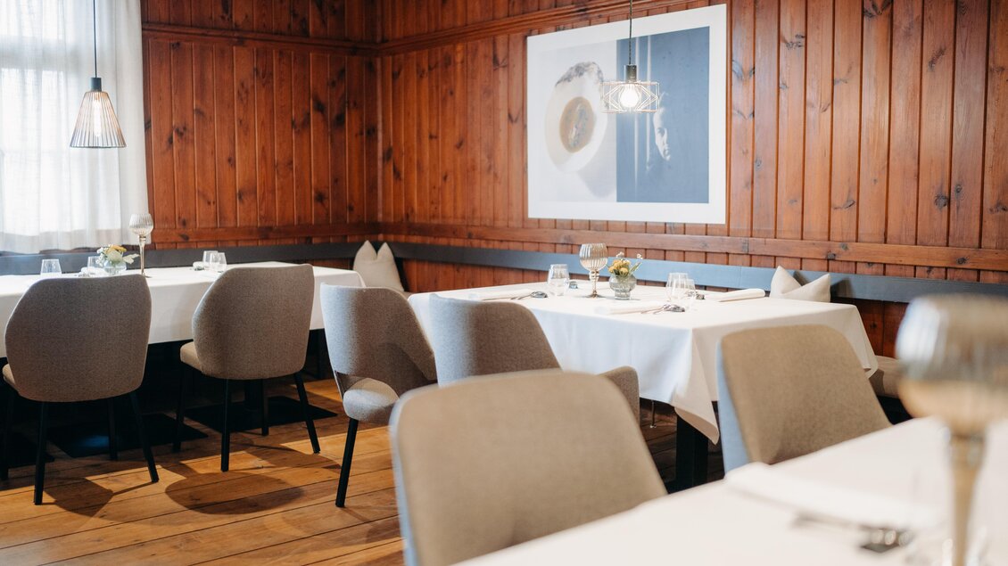 Ein elegantes Restaurant mit Holzwänden und modernen Möbeln. Die Tische sind stilvoll gedeckt und an der Wand hängt ein Kunstwerk. | © Hutter