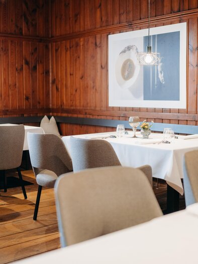 An elegant restaurant with wooden walls and modern furniture. The tables are stylishly set and a piece of artwork hangs on the wall. | © Hutter