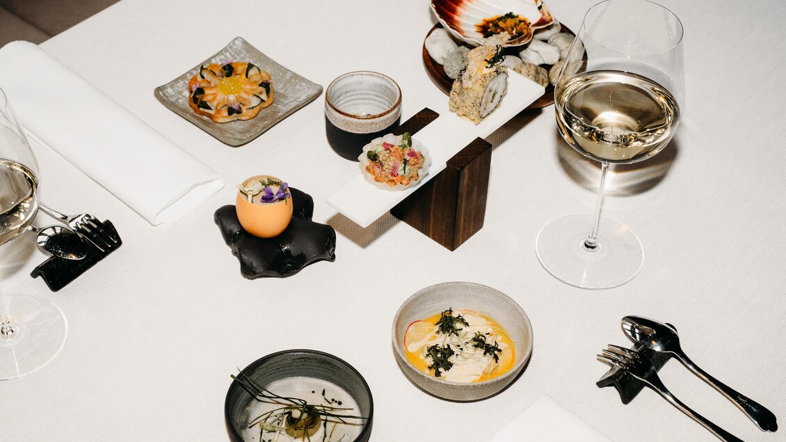 Ein elegantes Tischarrangement mit verschiedenen feinen Speisen und Getränken. Dazu gehören asiatische Häppchen, Meeresfrüchte und Wein in stilvollen Gläsern. | © Hutter