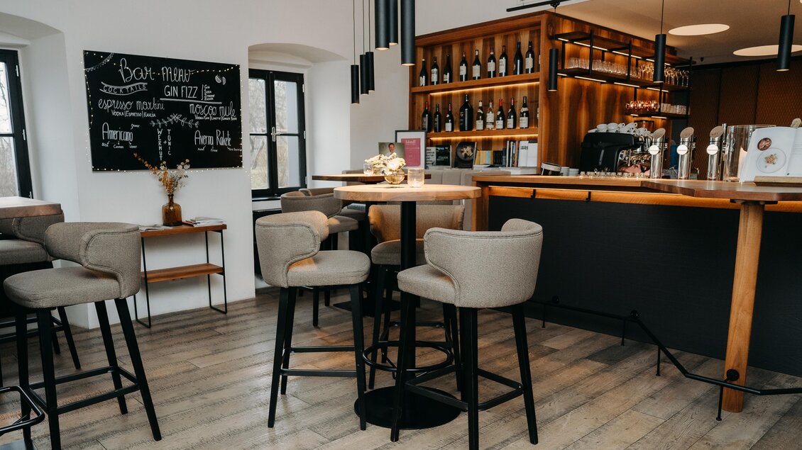 Eine gemütliche Bar mit modernen Stühlen und einer eleganten Theke. An der Wand befindet sich eine Tafel mit Informationen und Angeboten. | © Hutter