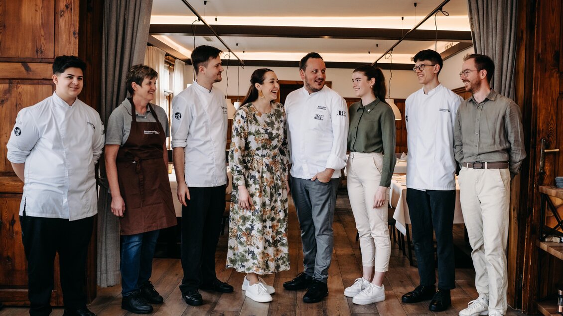 Eine Gruppe von acht Personen steht in einem Restaurant. Sie tragen verschiedene Kochuniformen und lächeln freundlich zueinander. | © Hutter
