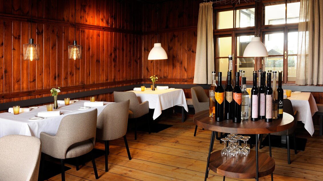 Ein gemütliches Restaurant mit Holzdekor und eleganten Tischen. Im Vordergrund stehen Weinflaschen auf einem Tisch. | © Apresvino Josef Krassnig
