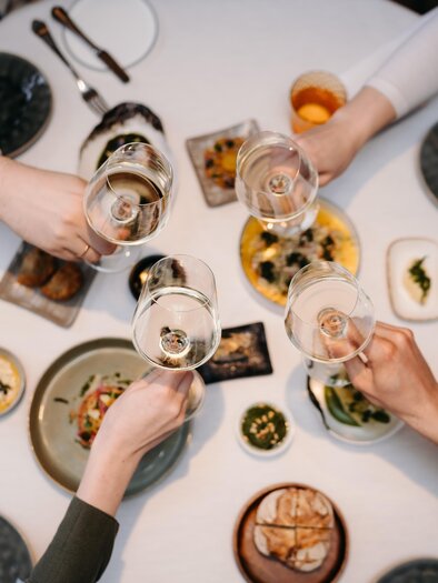 A festively set table with various dishes and drinks. Several hands are raising glasses in a toast.