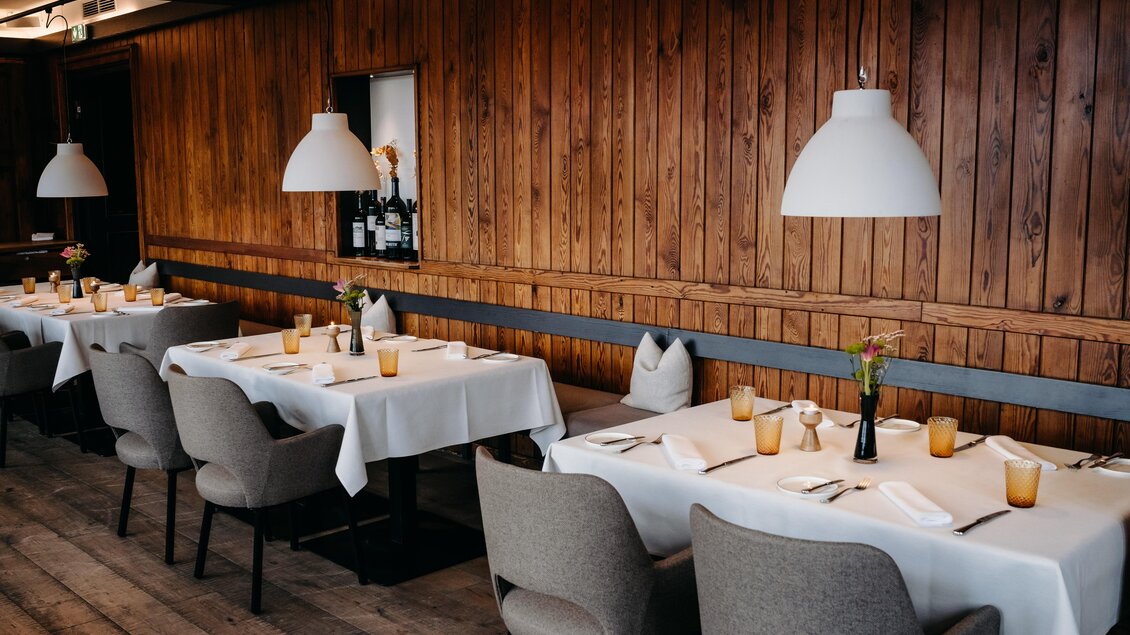 Ein elegantes Restaurant mit Holzwänden und stilvollen Tischgedecken. Die Tische sind geschmückt mit Blumen und Kerzen in einem einladenden Ambiente. | © Hutter