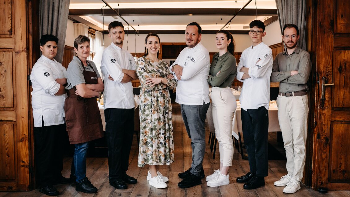 Eine Gruppe von acht Personen steht in einem eleganten Restaurant. Sie tragen Küchenkleidung und lächeln, während sie in die Kamera schauen. | © Hutter