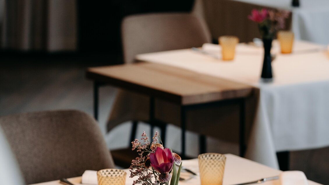 Ein stilvolles Restaurant mit elegant eingedeckten Tischen. Jede Tischdecke ist mit einer Vase und bunten Gläsern dekoriert.