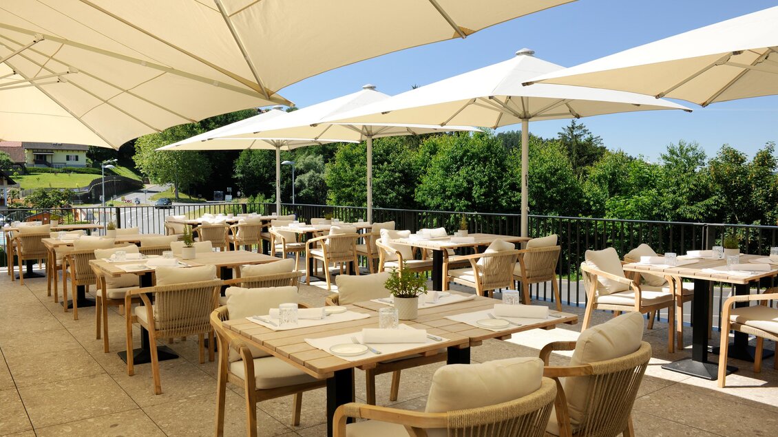 Ein modernes Restaurant mit außenliegenden Tischen und Sonnenschirmen. Die Umgebung ist grün und einladend, ideal für eine entspannte Mahlzeit im Freien. | © Schlosskeller Südsteiermark