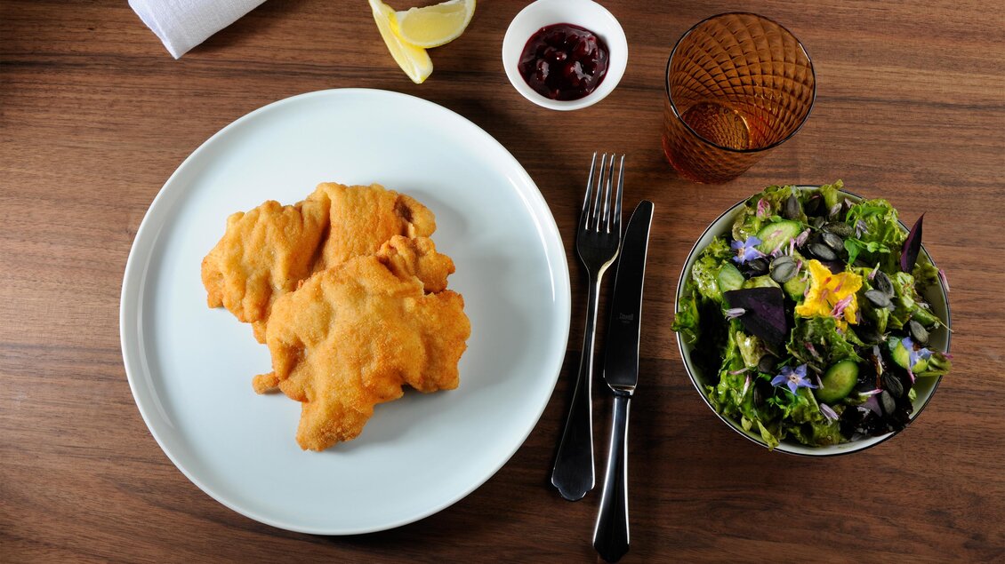 Ein Teller mit knusprig friedenen Fillets, begleitet von einem frischen Salat und einer Zitrone. Daneben befinden sich eine kleine Schüssel mit Sauce und ein Getränk. | © Schlosskeller Südsteiermark