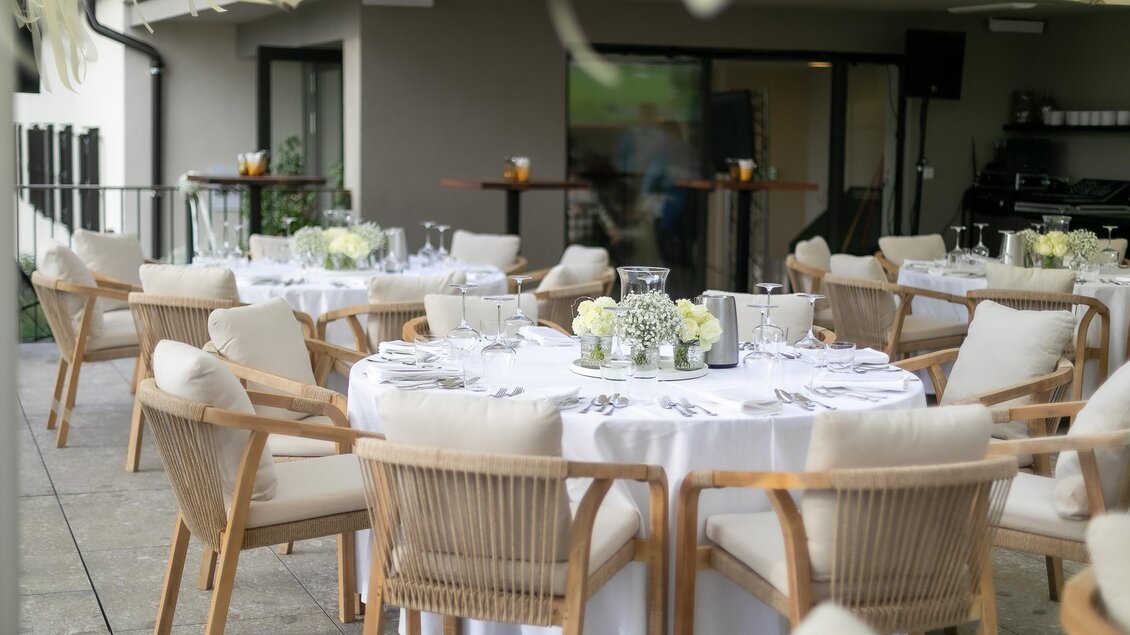Ein eleganter Tisch im Freien, schön gedeckt mit Blumenarrangements. Die Umgebung ist modern und einladend. | © Schlosskeller Südsteiermark