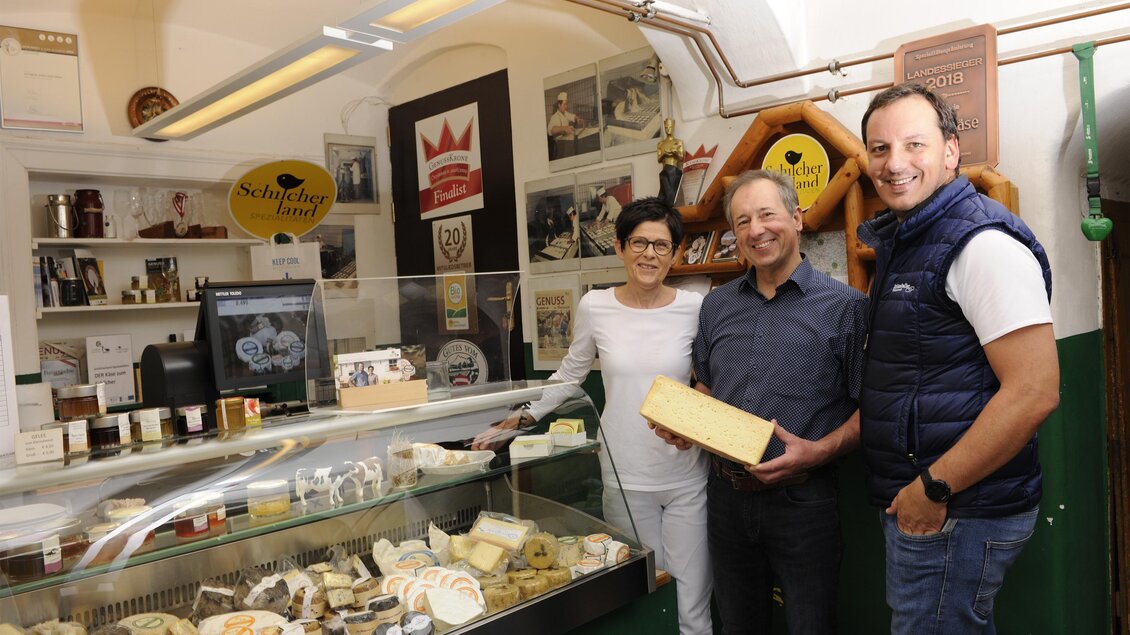 Ein Geschäft mit verschiedenen Käsesorten und freundlichen Verkäufern. Zu sehen sind drei Personen, die zusammen mit Käse und Aussicht im Laden posieren. | © Schlosskeller Südsteiermark