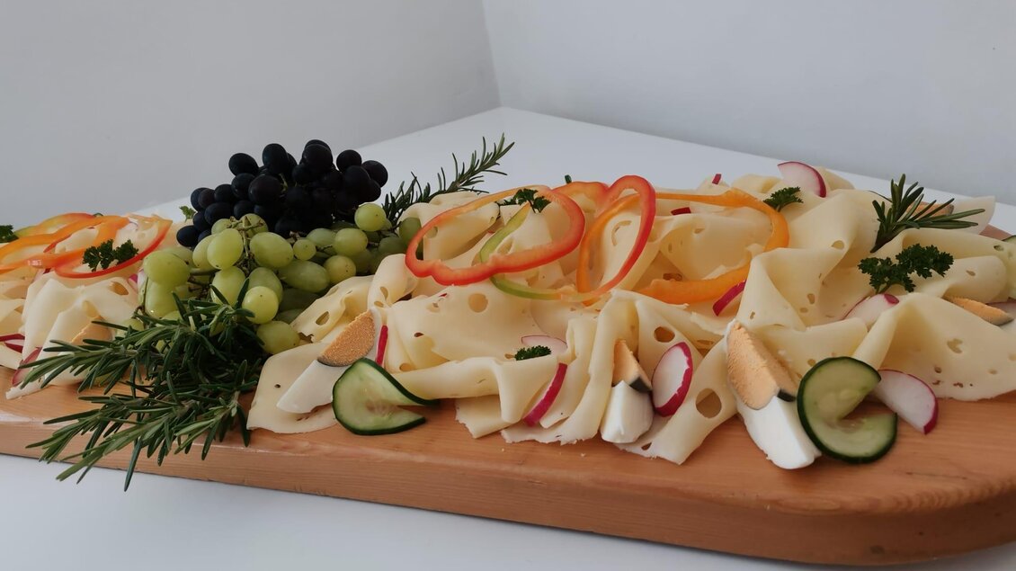 Eine schön angerichtete Käseplatte mit verschiedenen Käsesorten, Trauben und frischem Gemüse. Darüber hinaus sind bunte Paprikastreifen und Kräuter dekorativ platziert. | © Schlosstaverne