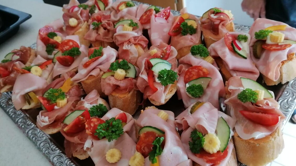 Eine Platte mit belegten Brötchen, garniert mit Schinken, Gemüse und frischen Kräutern. Die Snacks sind farbenfroh und appetitlich angerichtet. | © Schlosstaverne