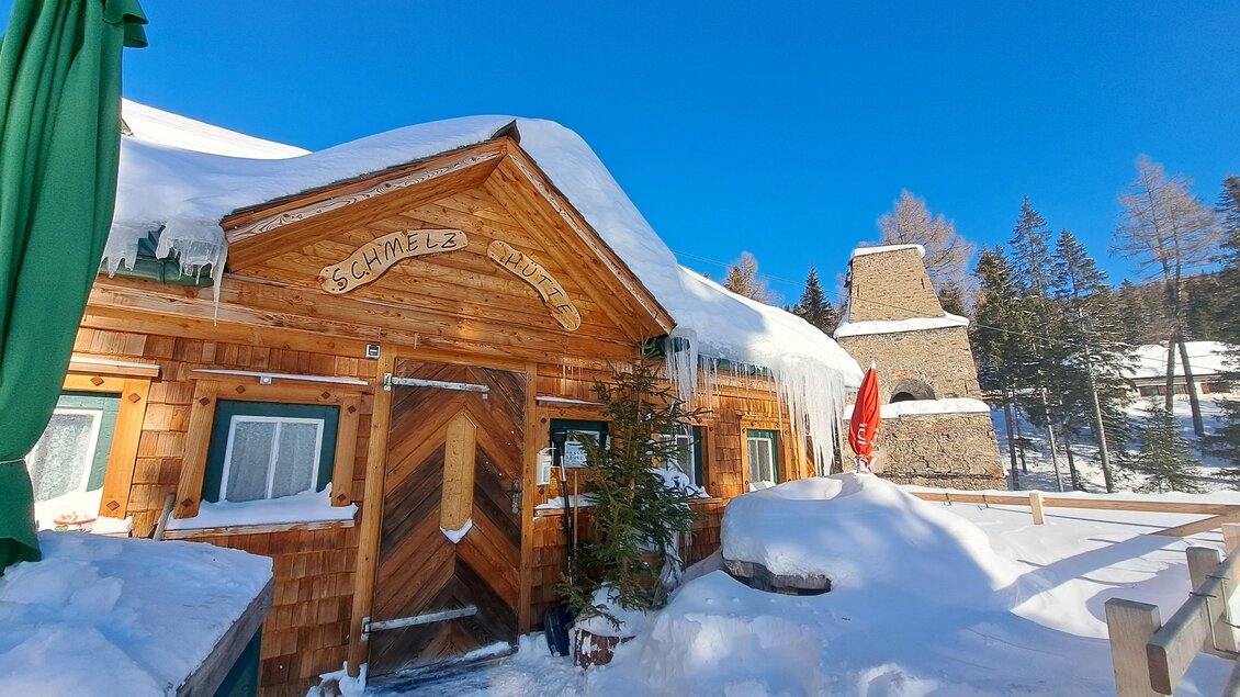 Eine gemütliche Holzhütte im Schnee, umgeben von verschneiten Bäumen und klarem blauen Himmel. Die Hütte hat ein charmantes, rustikales Design. | © Claudia Bachler