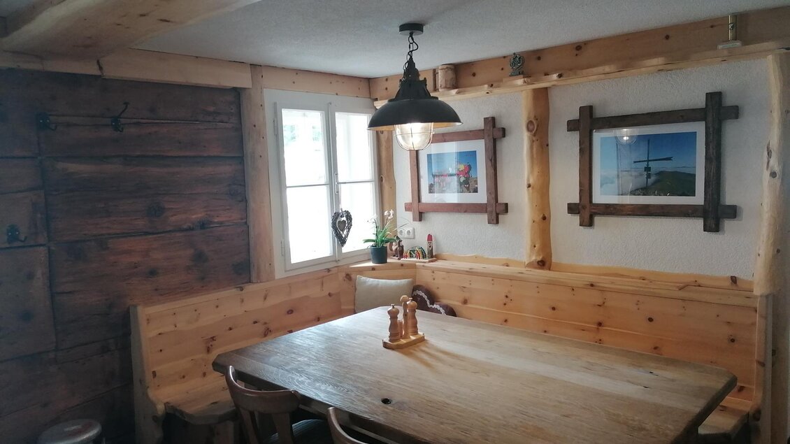 Ein gemütlicher Raum mit Holzwänden und einem großen Tisch. An den Wänden hängen einige Bilder, und das Licht hängt von einer stilvollen Lampe. | © Herbert Schönhart