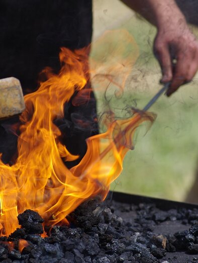Ein Feuer mit flammenden Glut und glühender Kohle. Eine Hand hält einen Hammer, bereit zum Schmieden. | © Pixabay