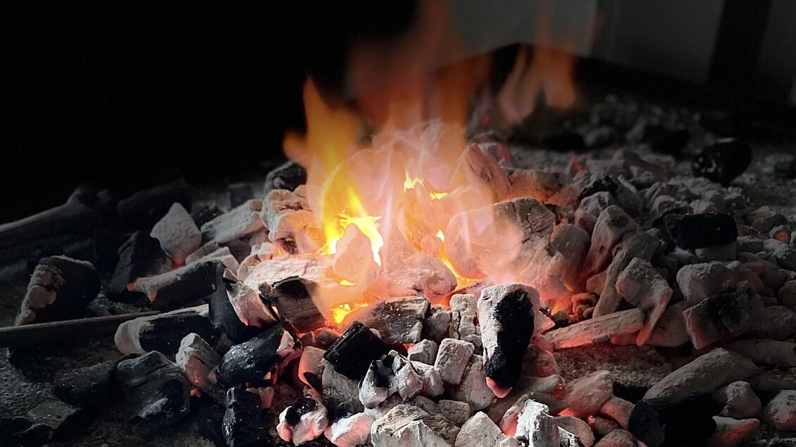 Ein brennendes Feuer auf einer Kohlenbasis. Die Flammen leuchten orange und rot auf dem grauen Kohlenhaufen. | © Kurt Forstner