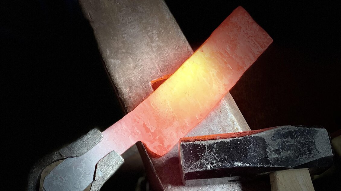 Ein glühendes Metallstück wird bearbeitet. Werkzeug und Anvil sind im Vordergrund sichtbar. | © Kurt Forstner
