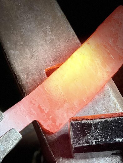 A glowing piece of metal is being worked on. Tools and an anvil are visible in the foreground. | © Kurt Forstner