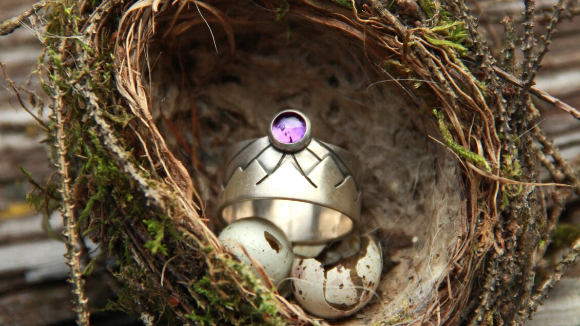 Ein kleines Nest mit einem Ring und einigen Eierschalen. Der Ring hat einen lila Stein und ist auf den Eierschalen platziert. | © Marlena Gerhart Schmuckgestalterin