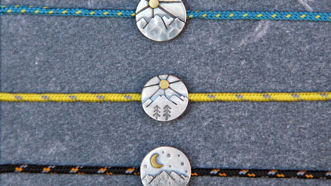 Drei Armbänder mit besonderen Anhängern in Kreisform. Jeder Anhänger zeigt eine unterschiedliche Landschaftsszene mit Bergen, Sonne und Mond. | © Marlena Gerhart Schmuckgestalterin