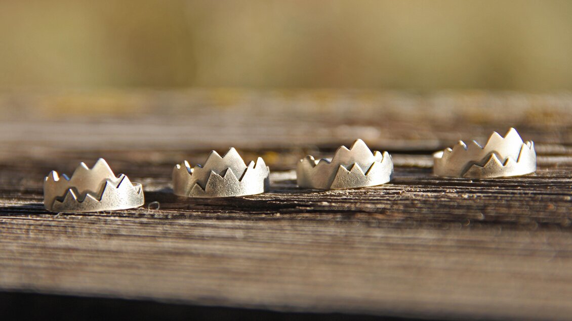 Fünf kleine Kronen aus Metall liegen auf einem Holzbrett. Die Formen sind einfach und kreativ gestaltet. | © Marlena Gerhart Schmuckgestalterin
