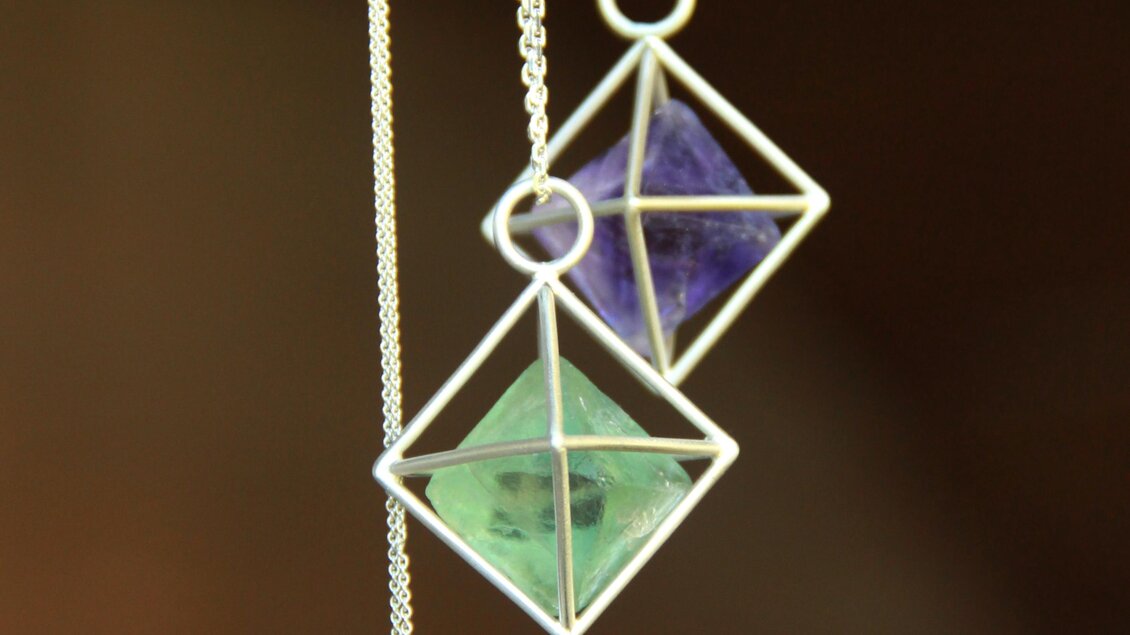 Drei geschmackvolle Anhänger in Form von Pyramiden hängen an einer Kette. Die Anhänger sind in verschiedenen Farben, darunter Grün und Lila, gestaltet. | © Marlena Gerhart Schmuckgestalterin