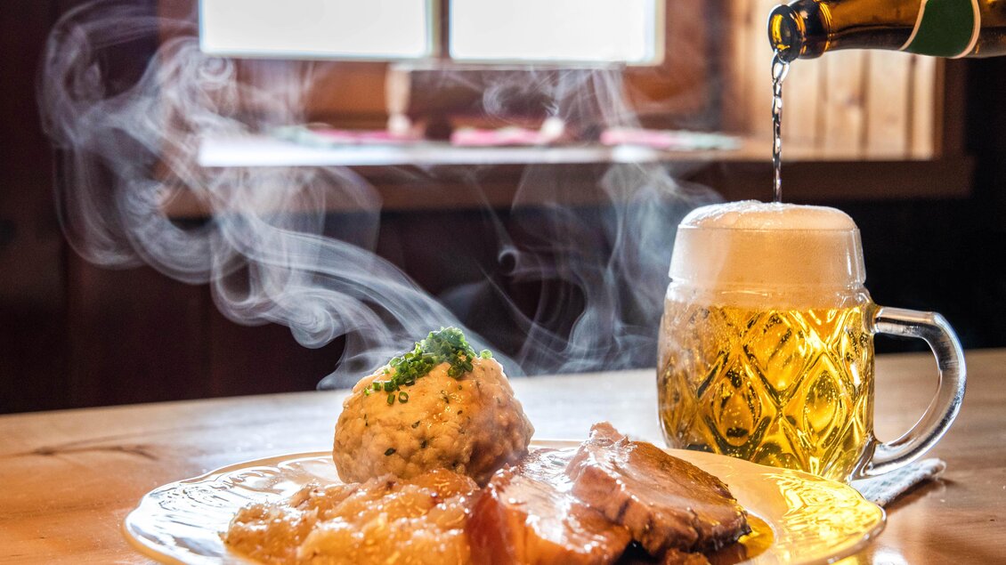Ein frisch zubereitetes Gericht mit Fleisch, Knödeln und einer dampfenden Soße. Daneben wird ein großes Bier in einem Glaskrug eingeschenkt. | © Corinna Harrer Fotografie