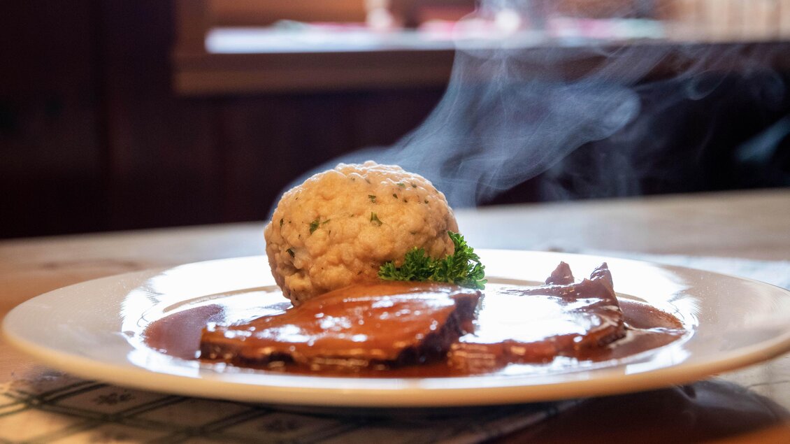 Ein köstliches Gericht mit zartem Fleisch und einer dampfenden Beilage aus Knödel. Dazu frische Kräuter auf einem weißen Teller. | © Corinna Harrer Fotografie