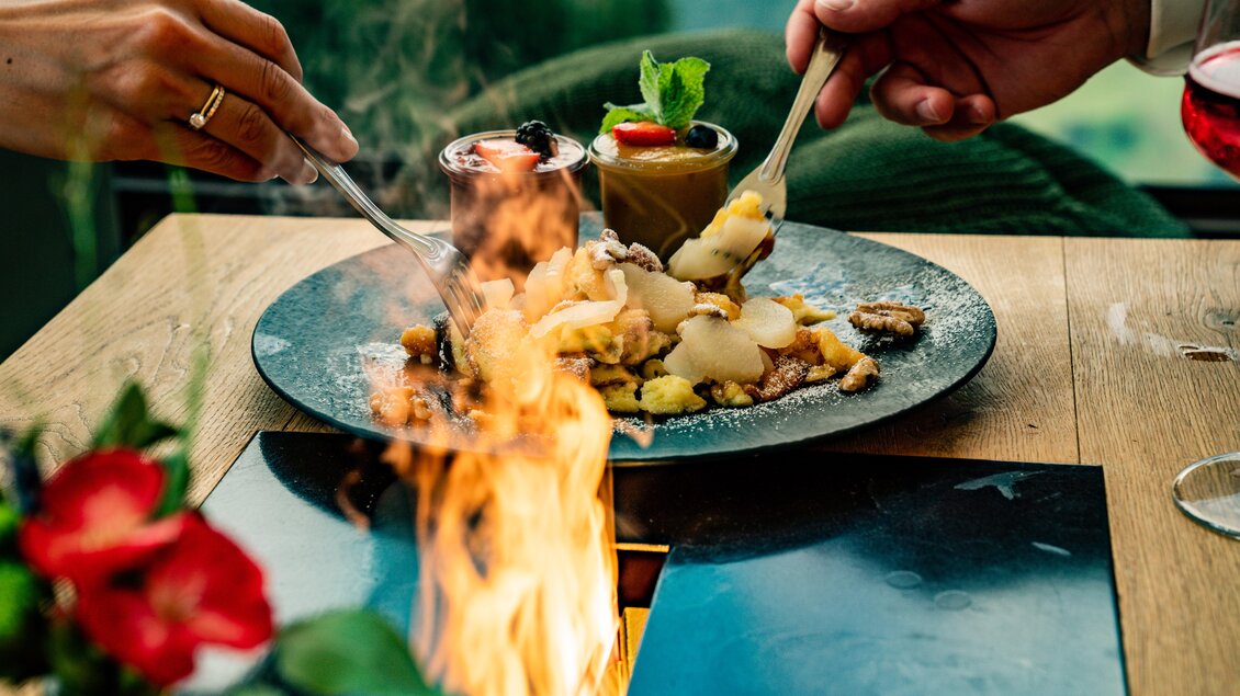 Ein köstlicher Teller mit verschiedenen Desserts und Früchten. Zwei Hände, die mit Löffeln zugreifen, während ein kleines Feuer im Hintergrund brennt. | © Christine Höflehner