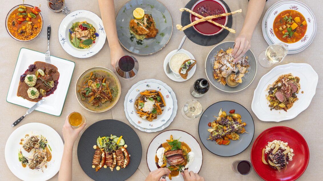 Ein festlich gedeckter Tisch mit verschiedenen Gerichten und Getränken. Hände greifen nach den Speisen, die farbenfroh und abwechslungsreich sind. | © Martin Huber