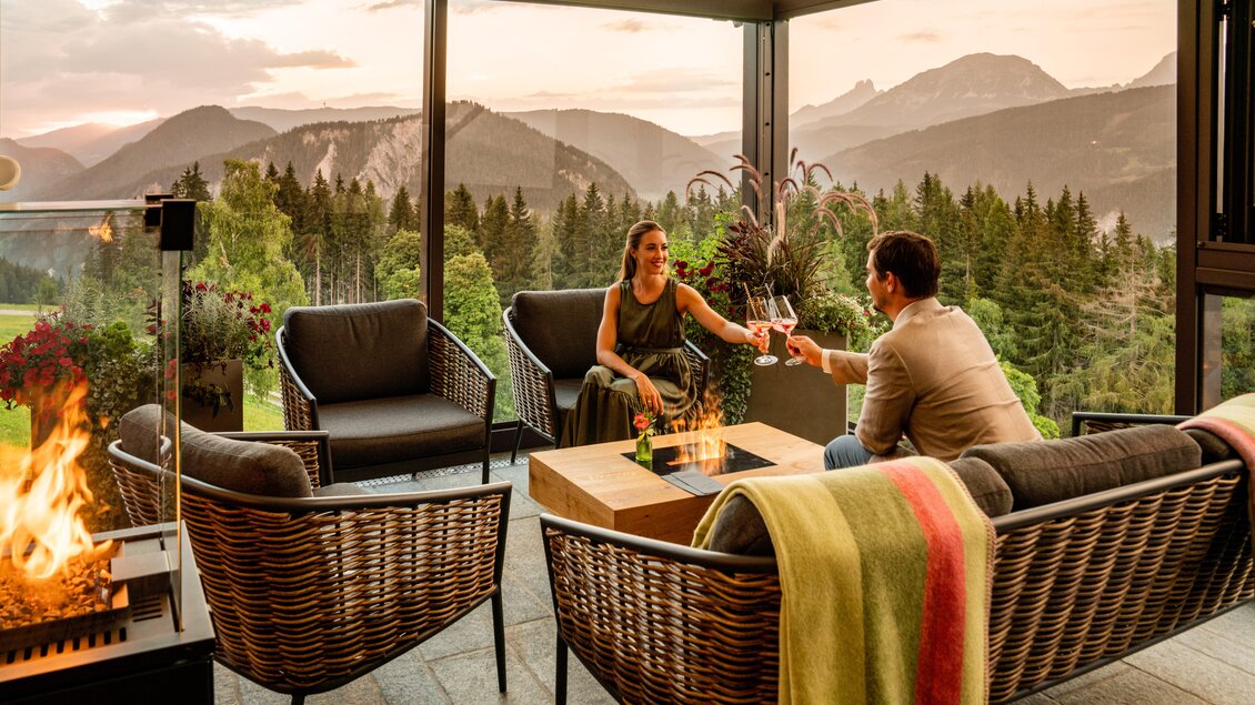 Eine gemütliche Terrasse mit einer Feuerstelle und Blick auf die Berge. Ein Paar genießt einen Abend mit Getränken und schöner Aussicht. | © Christine Höflehner