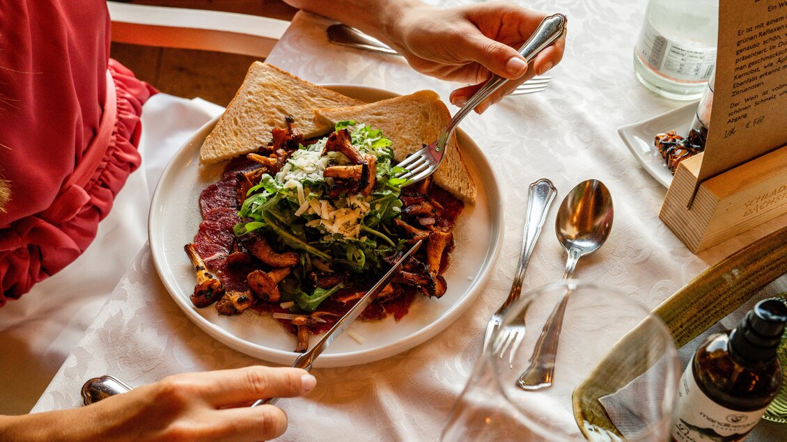 Ein Teller mit einer bunten Salatmischung, Rindfleisch und gerösteten Pilzen. Eine Person hält Besteck und ist bereit, zu essen. | © Christine Höflehner
