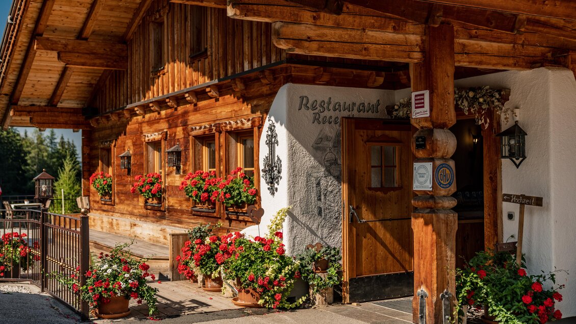 Ein traditionelles Holzhaus mit einem einladenden Eingang. Bunte Blumen schmücken die Fenster und den Außenbereich. | © Christine Höflehner