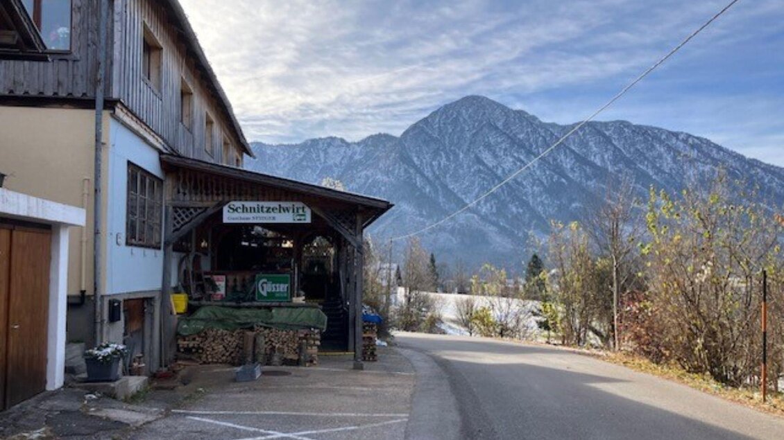 Ein gemütliches Gebäude mit einem Bistro-Schild steht an einer Straße. Im Hintergrund erheben sich schneebedeckte Berge unter einem klaren Himmel. | © TVB_Ausseerland Salzkammergut_Heike Temmel