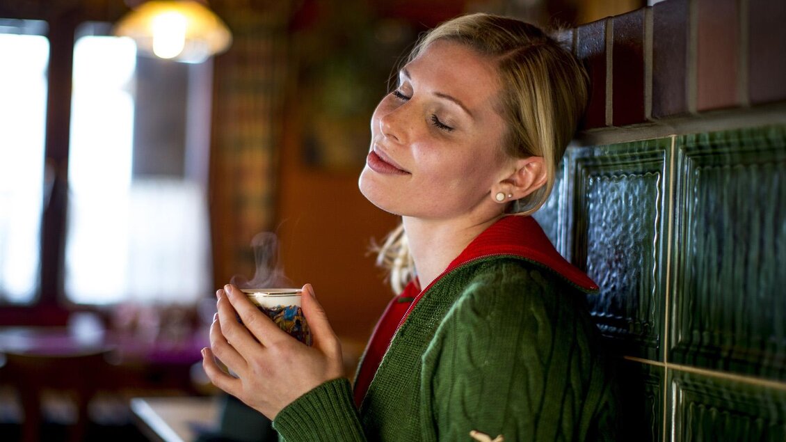 Eine Frau genießt ein Getränk in einem gemütlichen Raum. Sie trägt einen grünen Pullover und sieht zufrieden aus. | © TVB Ausseerland - Salzkammergut_Tom Lamm