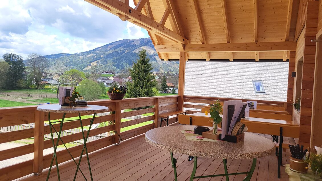 Ein gemütlicher Balkon mit Holzdecken und Sicht auf die Berge. Zwei Tische stehen auf dem Holzboden, umgeben von einer schönen Landschaft. | © TV Hochsteiermark