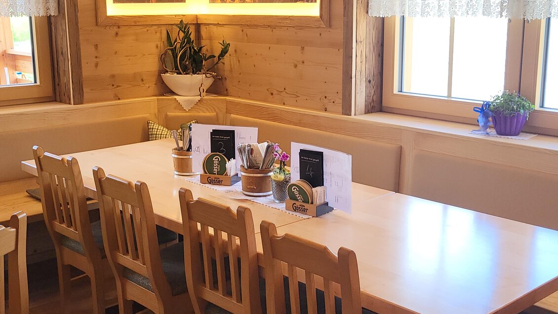 Eine gemütliche Restaurant-Ecke mit einem großen Holztisch und bequemen Stühlen. Die Fenster lassen viel Tageslicht herein und Pflanzen sorgen für eine einladende Atmosphäre. | © TV Hochsteiermark