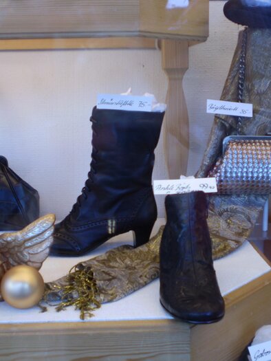 Schuhgeschäft mit verschiedenen Stiefeln in einer Auslage. Neben den Stiefeln sind dekorative Elemente wie Engel und Taschen zu sehen. | © Schuhhaus Scharzenberger