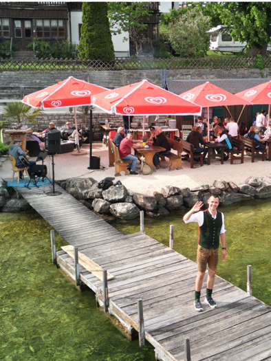 Ein schöner Steg führt zu einem gemütlichen Restaurant am Wasser. Gäste sitzen unter roten Schirmen und genießen die Zeit am See. | © Christoph Knappe