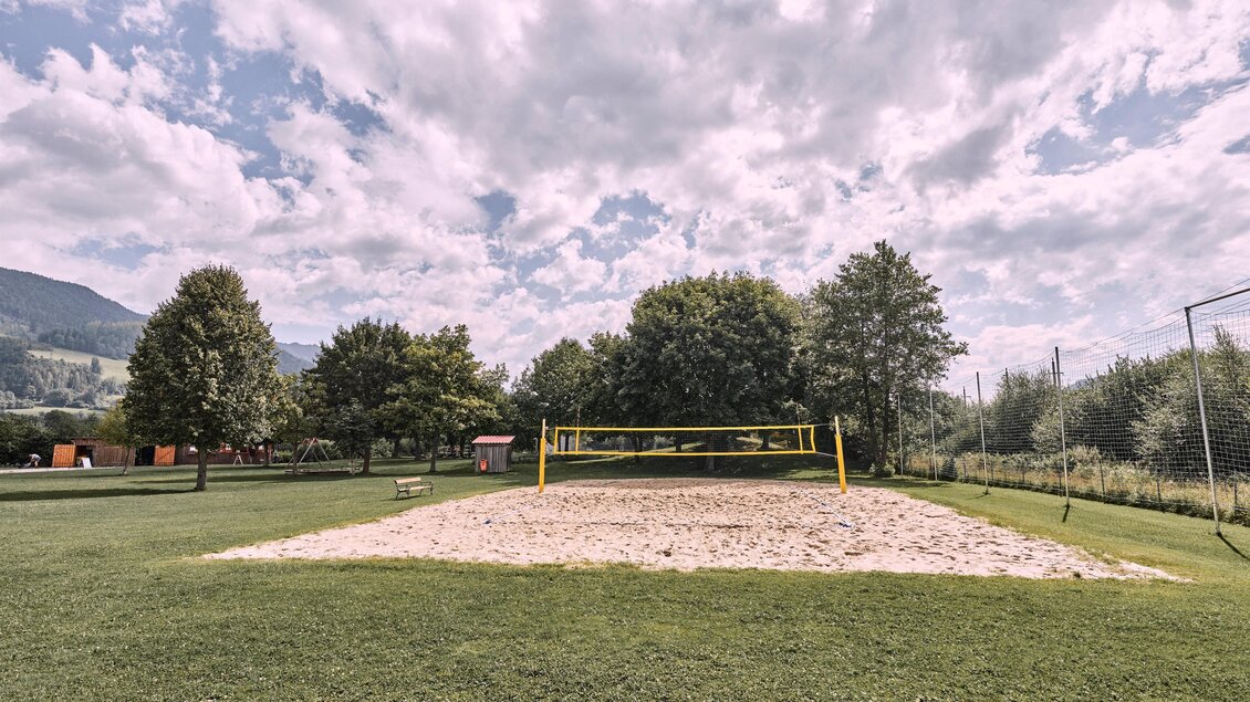 Ein Sandvolleyballplatz in einer grünen Umgebung mit Bäumen und einer bewölkten Himmel. Die Fläche ist gut gepflegt und bietet Platz für sportliche Aktivitäten. | © Thomas Sattler