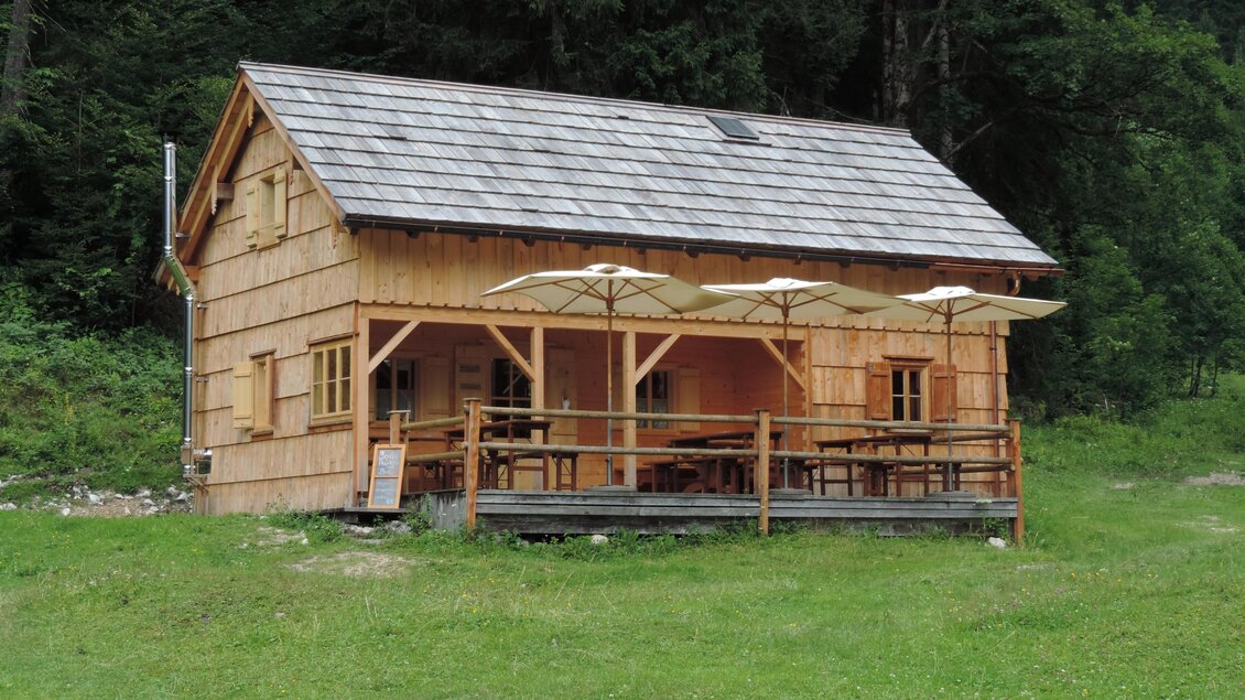 Ein gemütliches Holzhaus mit einer Terrasse und Sonnenschirmen. Es liegt umgeben von grüner Wiese und Bäumen. | © Gertraud Kalss
