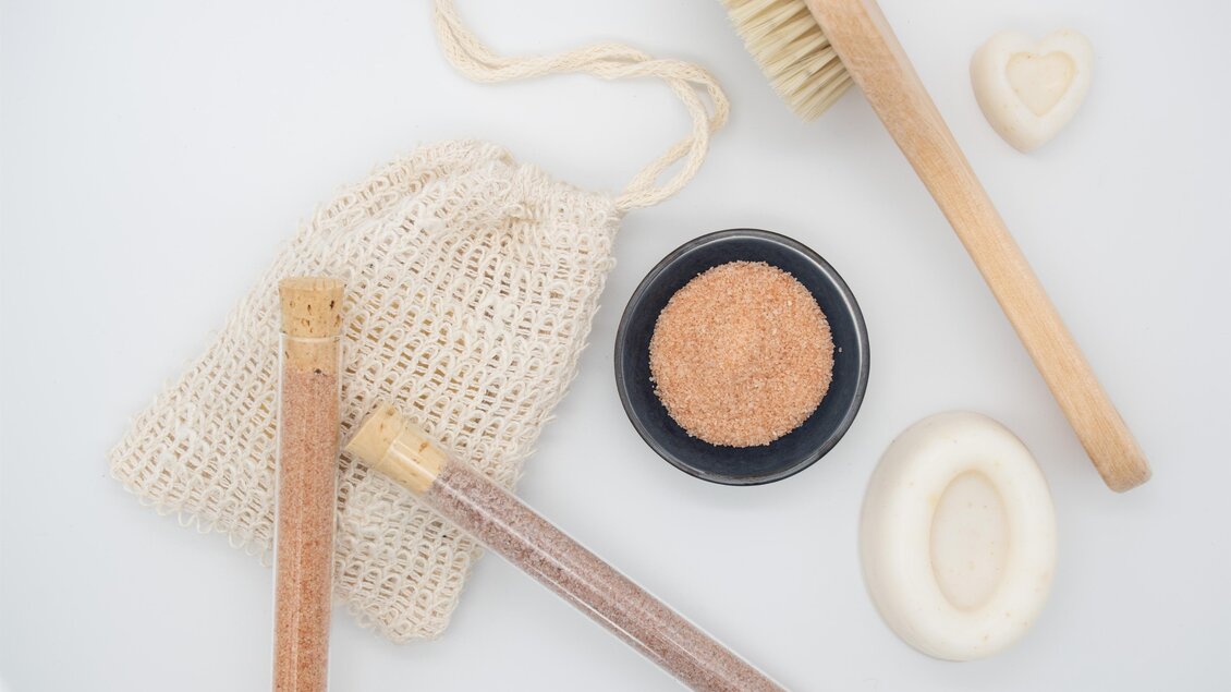 Eine angeordnete Auswahl an Hautpflegeutensilien, einschließlich einer Jutesack, Bürste und verschiedenen Peelings. Die Farben sind natürlich und beruhigend, ideal für ein Wellness-Erlebnis. | © lela. Design Studio