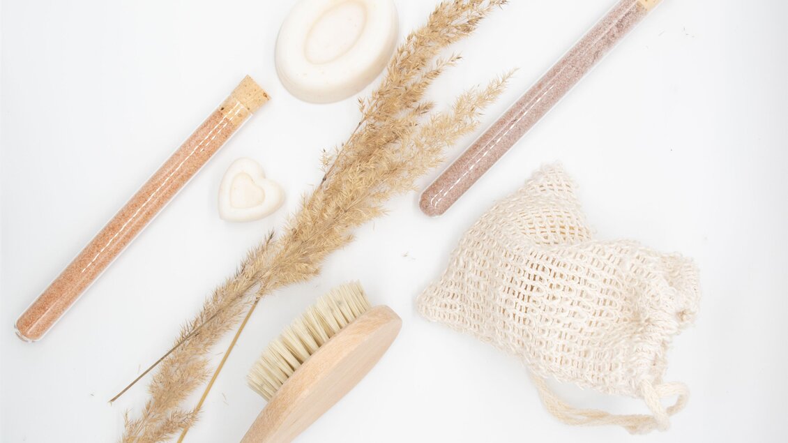 Eine entspannende Anordnung von natürlichen Schönheitsprodukten und Dekorationen. Zu sehen sind Bürsten, Seifen und Trockenblumen auf einem weißen Hintergrund. | © lela. Design Studio