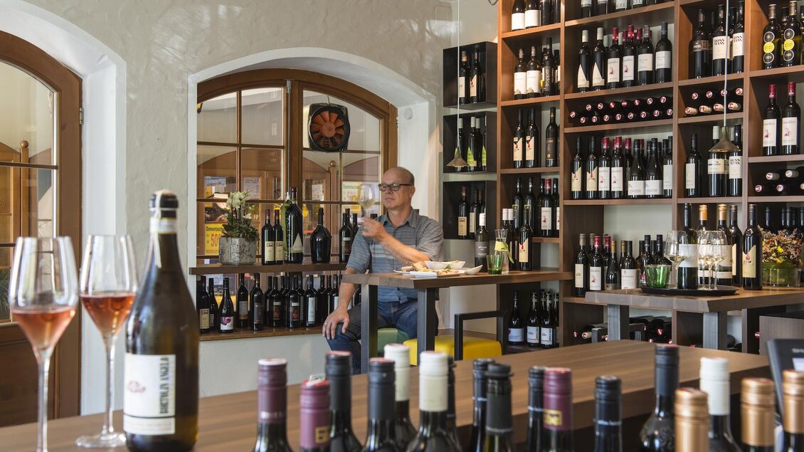 Ein gemütliches Weinlokal mit einem Mann, der an einer Bar sitzt. Im Hintergrund sind Regale mit verschiedenen Weinsorten zu sehen. | © Sissi´s Weinbar