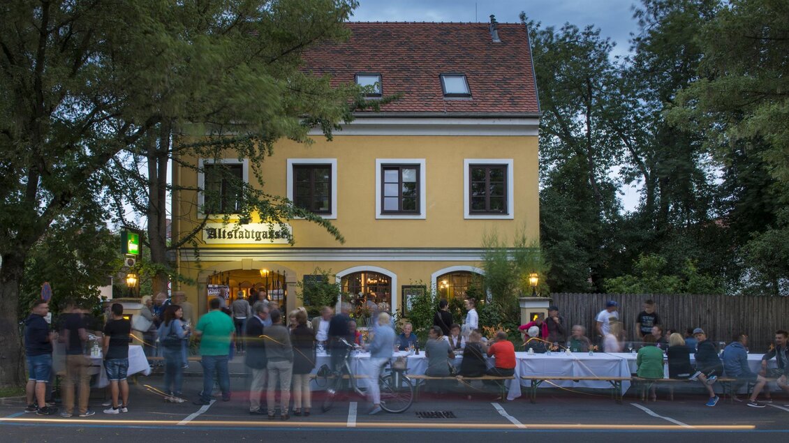 Ein lebhaftes Restaurant mit einer gelben Fassade und Außenbereich voller Menschen. Die Besucher genießen die Atmosphäre an einem warmen Abend. | © Sissi´s Weinbar
