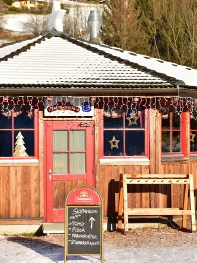 Ein gemütliches Holzhaus mit roter Tür und bunten Lichtern. Es ist mit Schnee bedeckt und liegt in einer winterlichen Umgebung. | © Anita Fössl